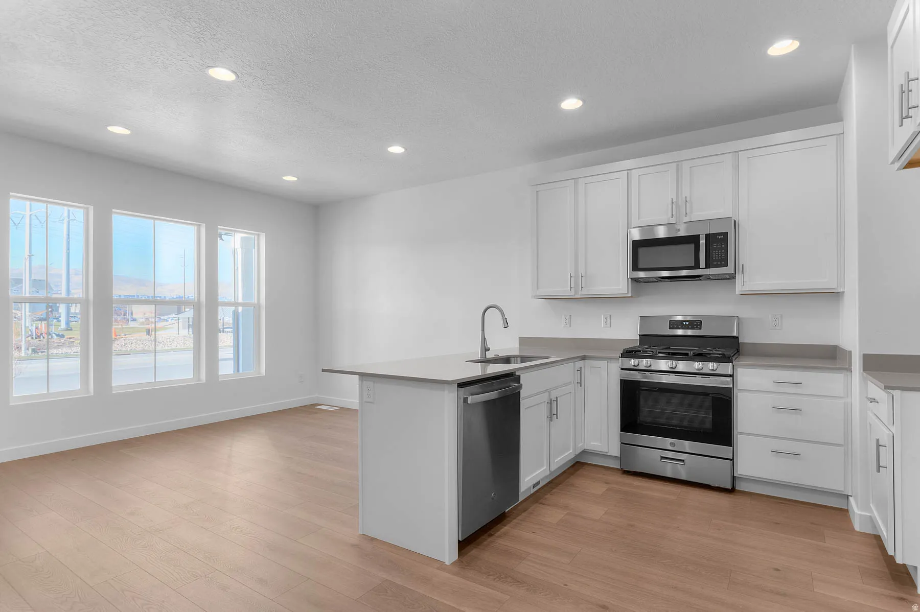 Contemporary kitchen featuring white cabinetry, stainless steel appliances, light countertops, a kitchen island with an integrated sink, and recessed lighting