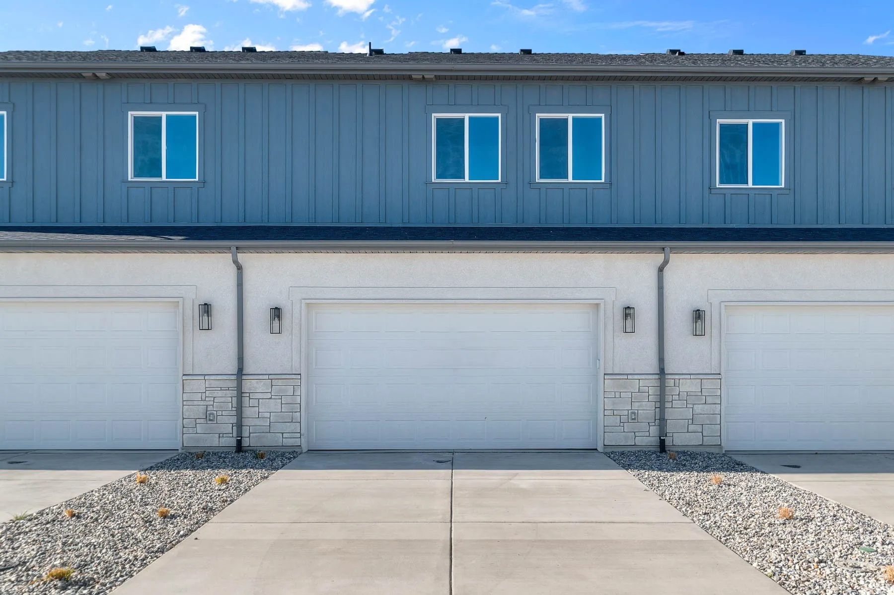 Building exterior featuring multiple garage doors, light blue board and batten siding, white stucco, and a stone facade