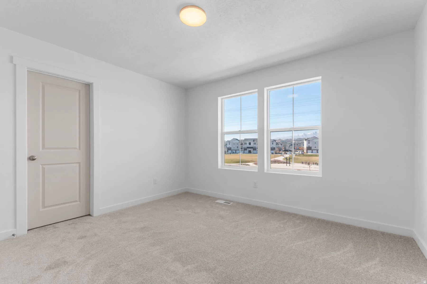 Bright room featuring two large windows, neutral carpet, a two-panel door, and a flush-mount ceiling light