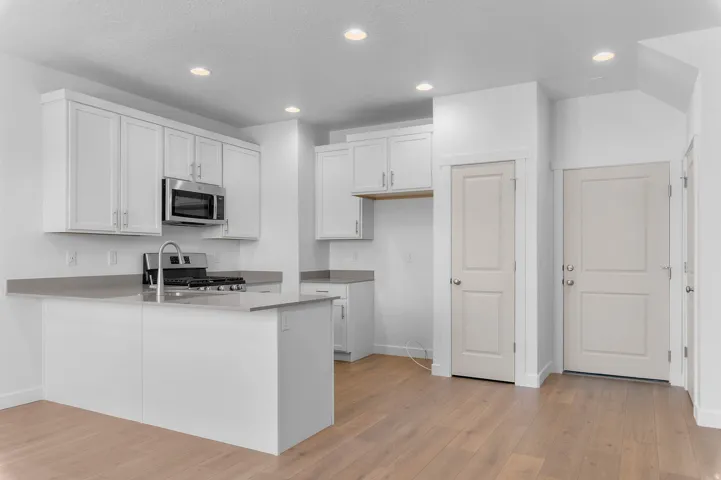 Contemporary kitchen featuring white cabinetry, stainless steel microwave, gas range, and a kitchen island with an integrated sink and chrome faucet