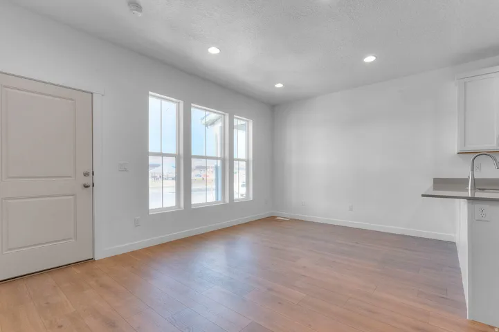 Open concept living space featuring wood-finish flooring, a white paneled door, three vertical windows, recessed lighting, and a kitchen peninsula with a stainless steel faucet and gray countertop