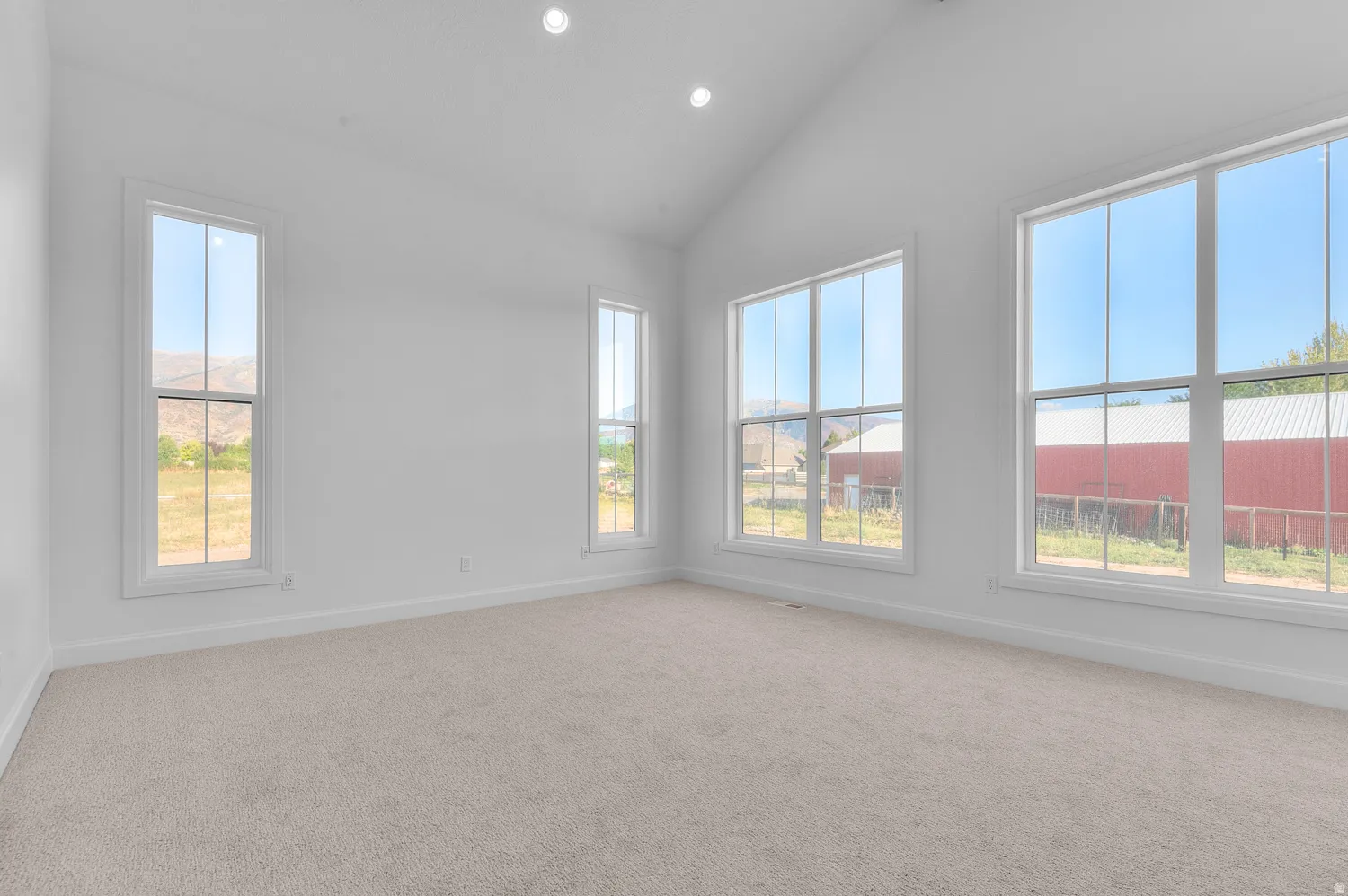 Vaulted ceiling room featuring recessed lighting, multiple large windows with white trim, light-colored carpeting, and white painted walls