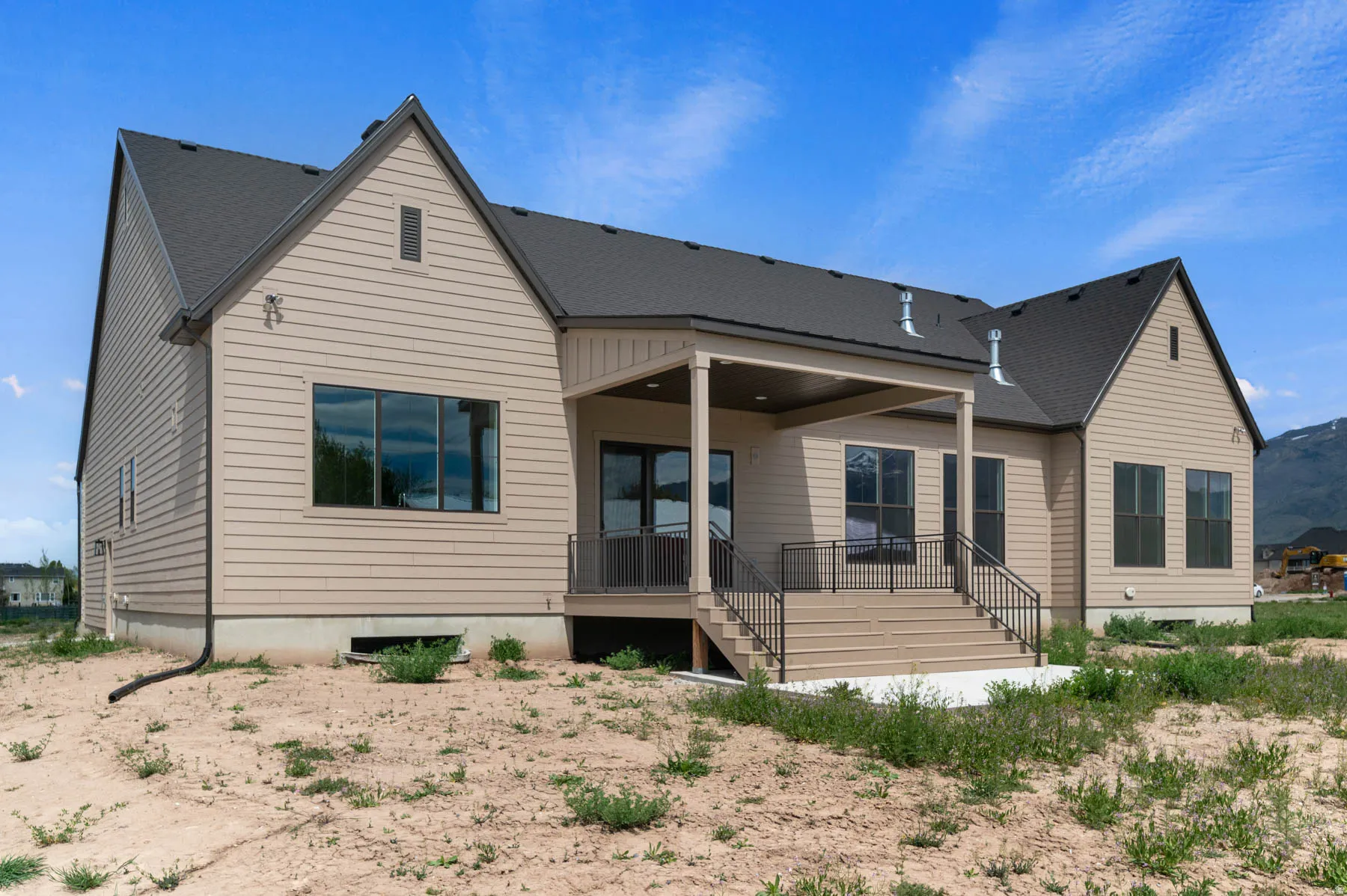 Rear exterior featuring a covered patio, composite decking, black metal railings, and tan horizontal siding