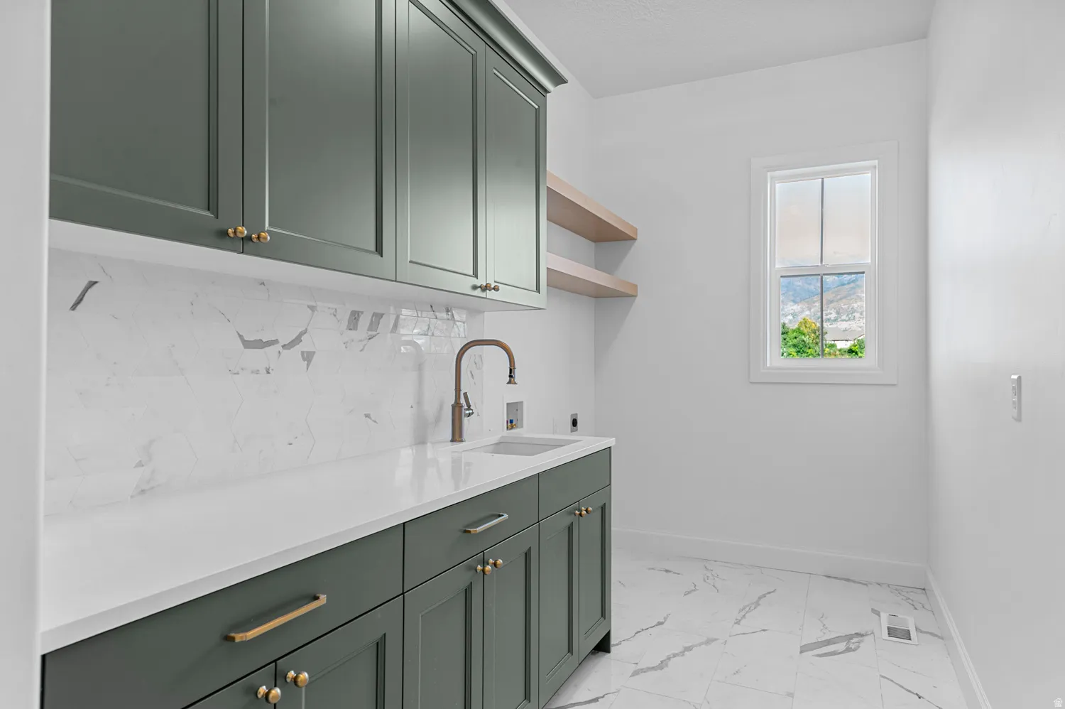 Laundry room with dark green cabinetry, white countertop, marble-look tile backsplash, and a window providing natural light