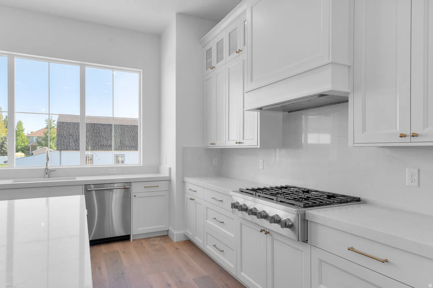 Bright kitchen featuring abundant white cabinetry, light countertops, wood-finish flooring, a stainless steel gas range, and an integrated dishwasher