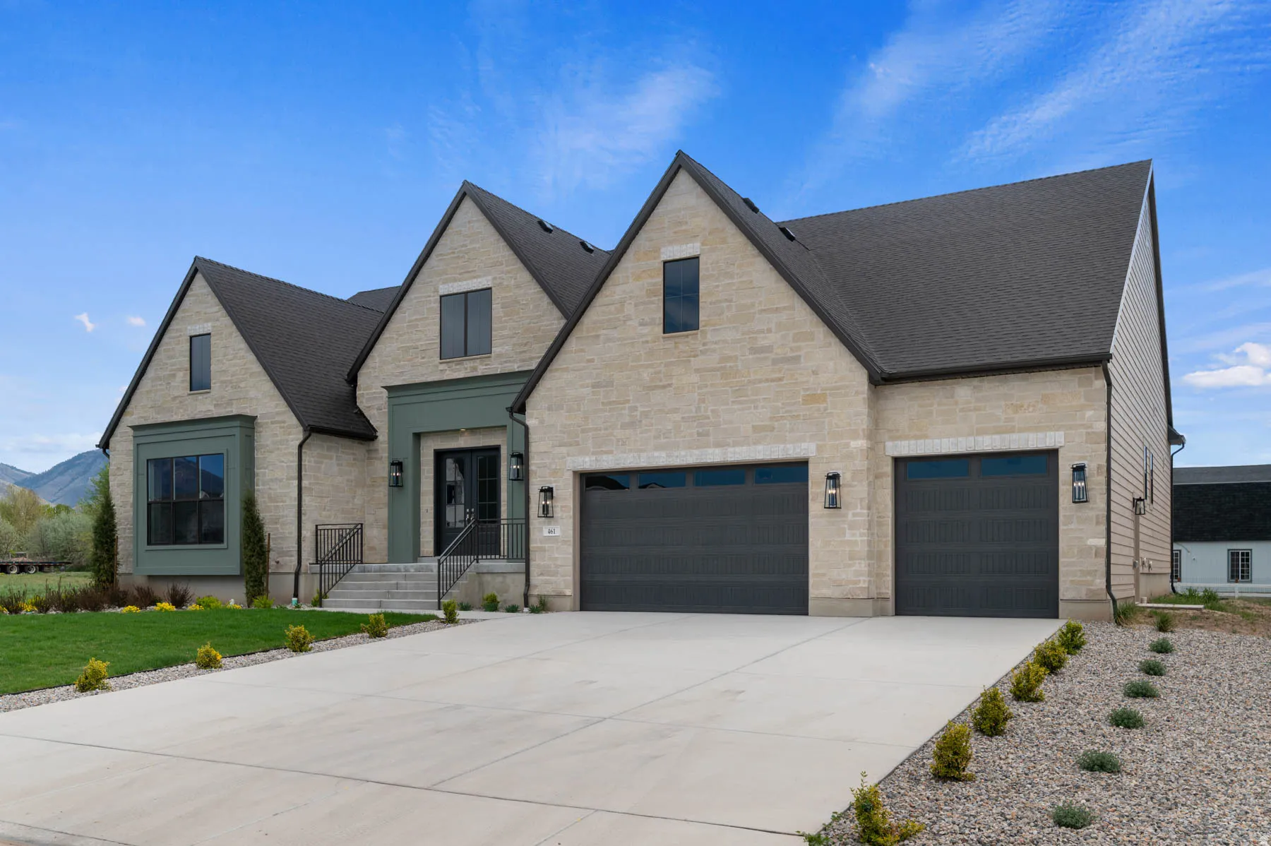 Stone facade residence featuring a two-car garage with dark paneled doors, a striking teal entry surround with double doors, and a prominent bay window