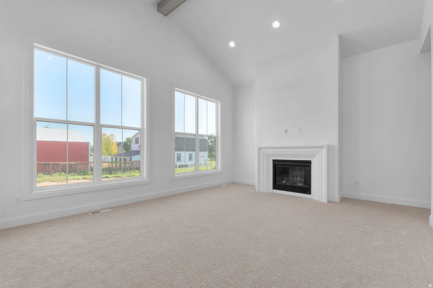 Spacious room featuring a vaulted ceiling with exposed beam, multiple large windows, recessed lighting, and a built-in fireplace with a white mantle