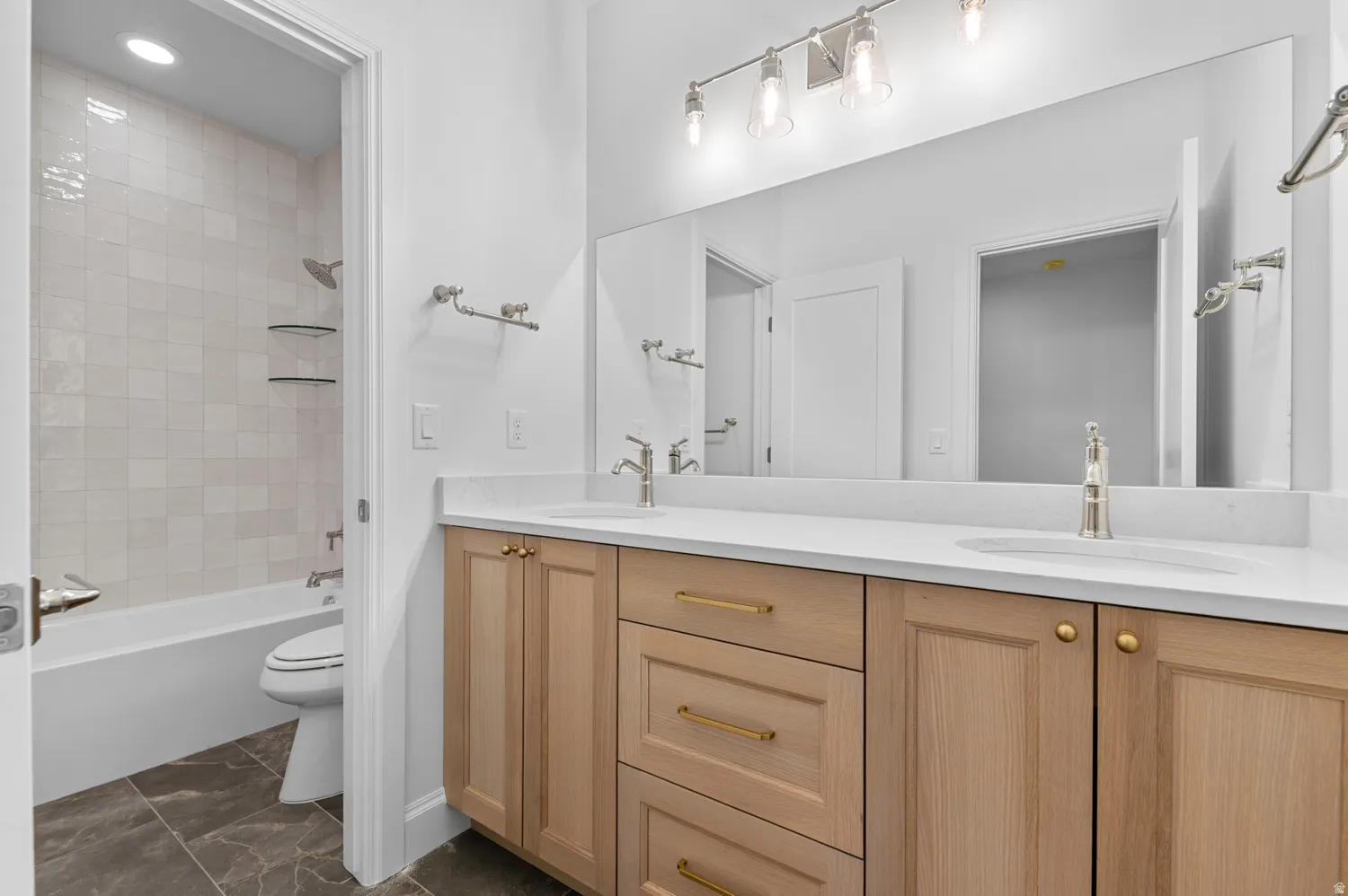 Contemporary bathroom featuring a double vanity with light wood cabinetry, white countertops, and dual undermount sinks