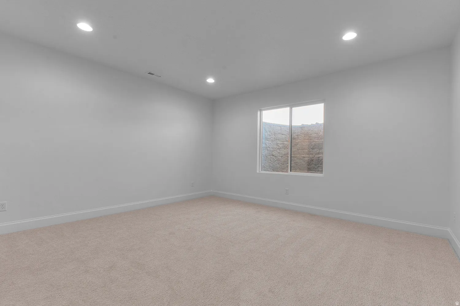 Spacious room featuring neutral carpet flooring, recessed lighting, and a window providing natural illumination
