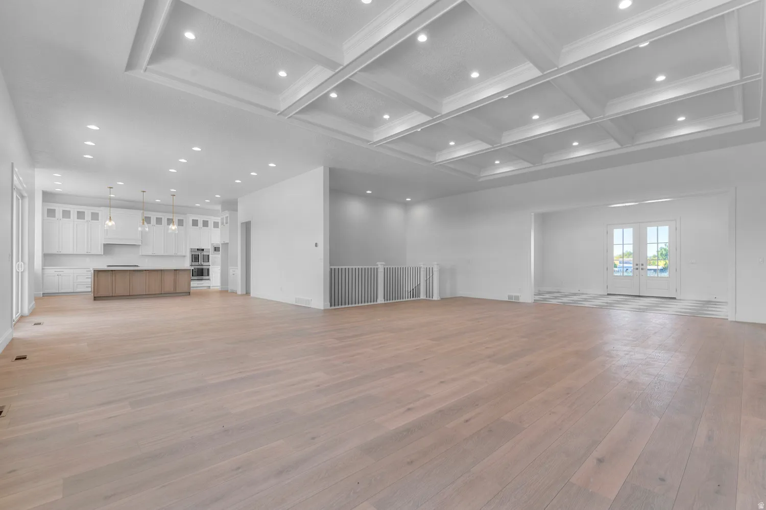 Expansive open-concept living space featuring light wood-finish flooring, a coffered ceiling with recessed lighting, and a modern kitchen