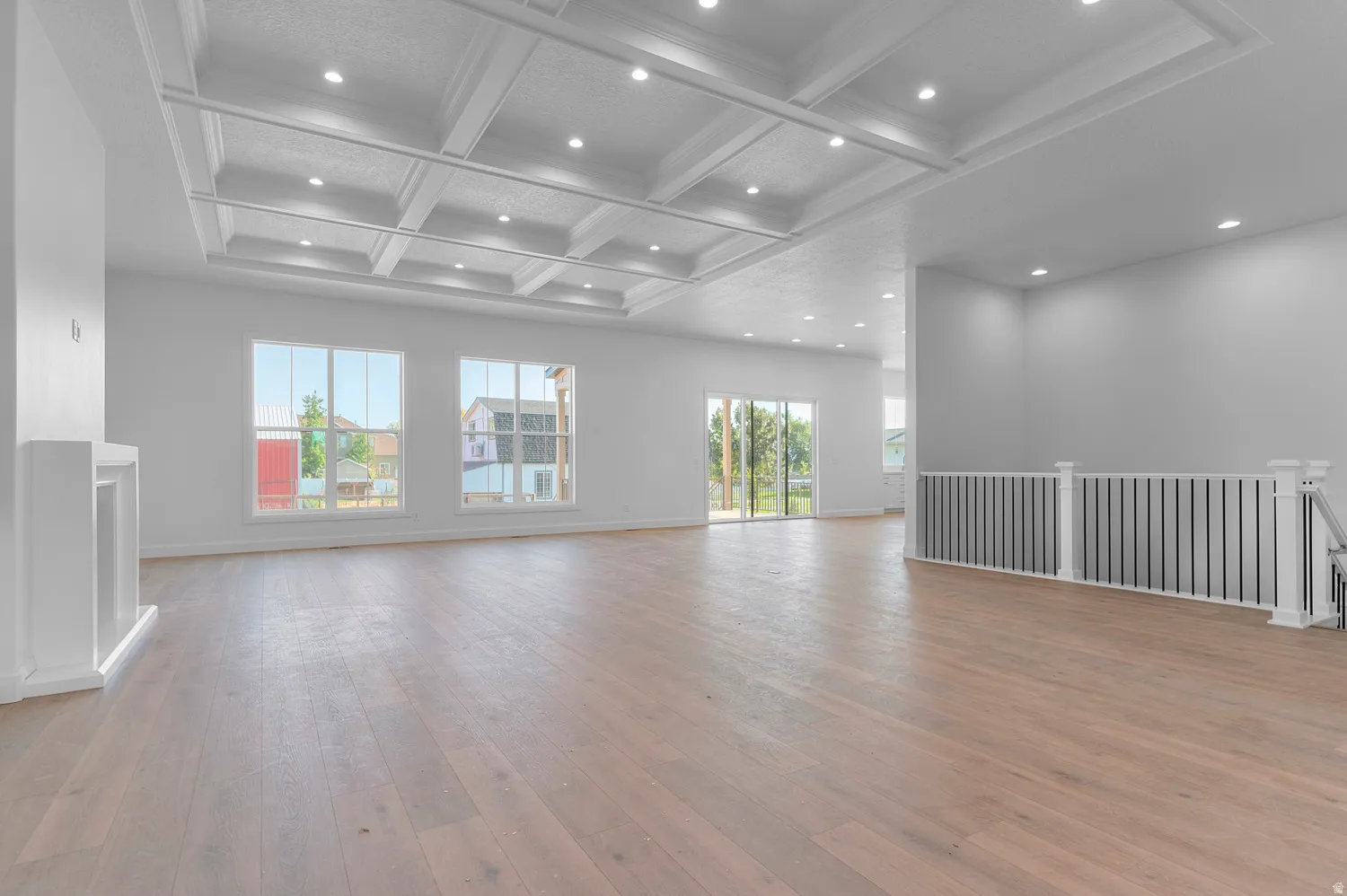Spacious interior featuring coffered ceilings with recessed lighting, light wood-finish flooring, multiple windows, a built-in fireplace mantle, and a staircase with a railing