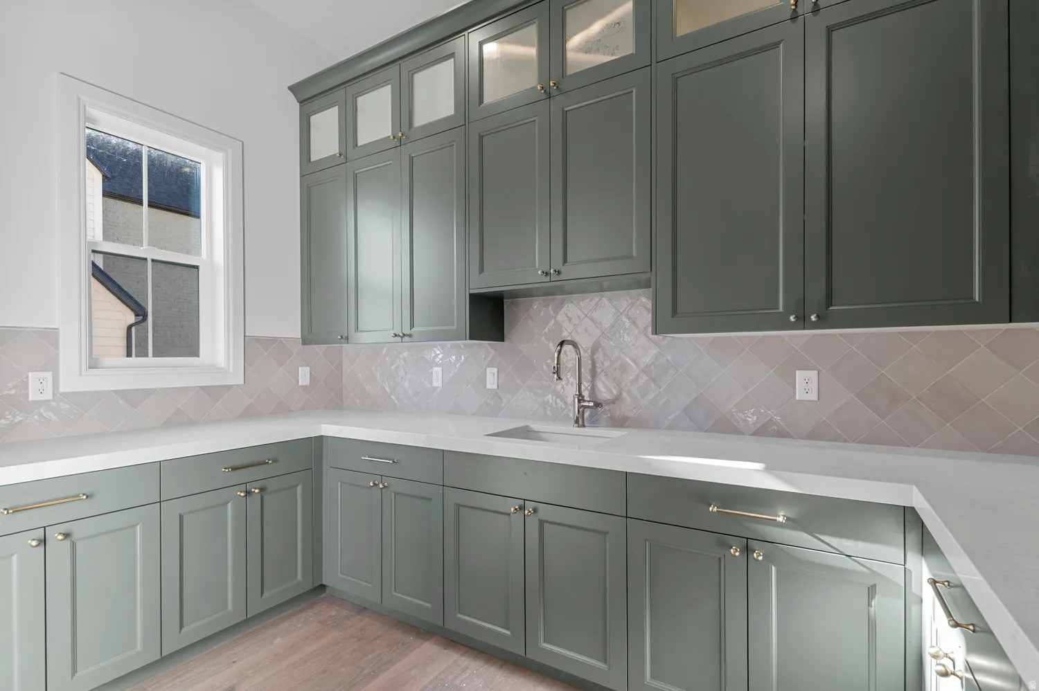 Kitchenette featuring sage green cabinetry, white countertops, square grid window, light-toned backsplash, and wood-finish flooring