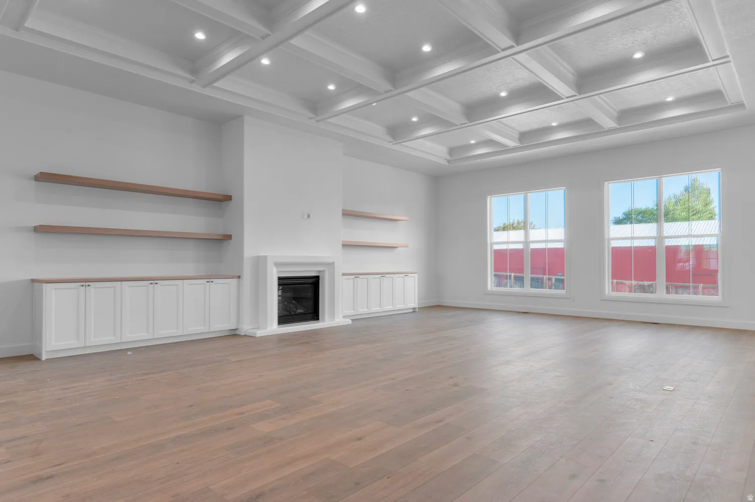 Spacious interior featuring a coffered ceiling with recessed lighting, light wood-finish flooring, and a fireplace with a white surround