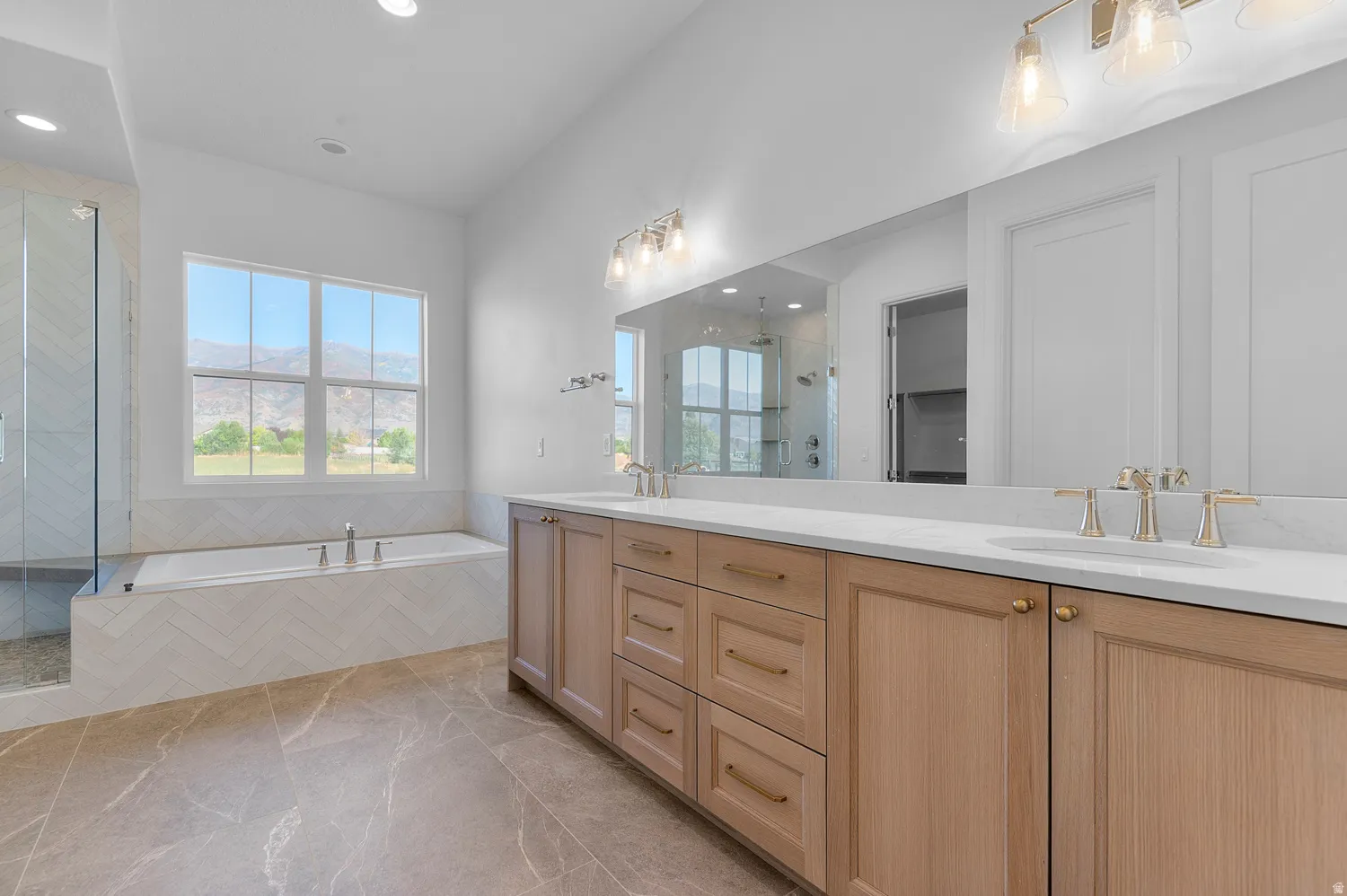 Spacious bathroom featuring a dual vanity with light wood cabinetry, white countertops, and gold-finish fixtures