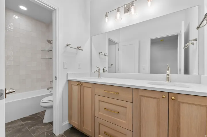 Contemporary bathroom featuring a double vanity with light wood cabinetry, white countertops, and dual undermount sinks