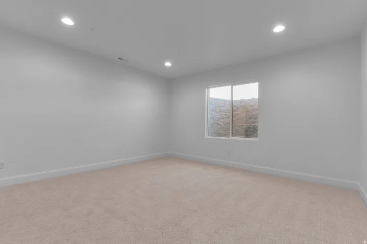 Spacious room featuring neutral carpet flooring, recessed lighting, and a window providing natural illumination