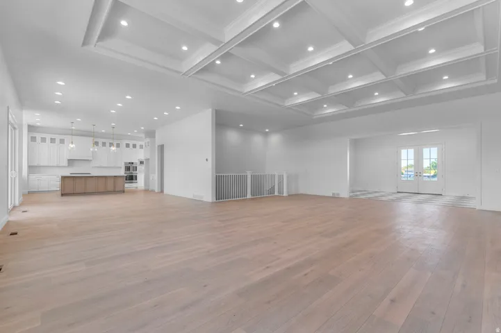 Expansive open-concept living space featuring light wood-finish flooring, a coffered ceiling with recessed lighting, and a modern kitchen