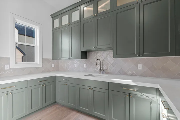 Kitchenette featuring sage green cabinetry, white countertops, square grid window, light-toned backsplash, and wood-finish flooring