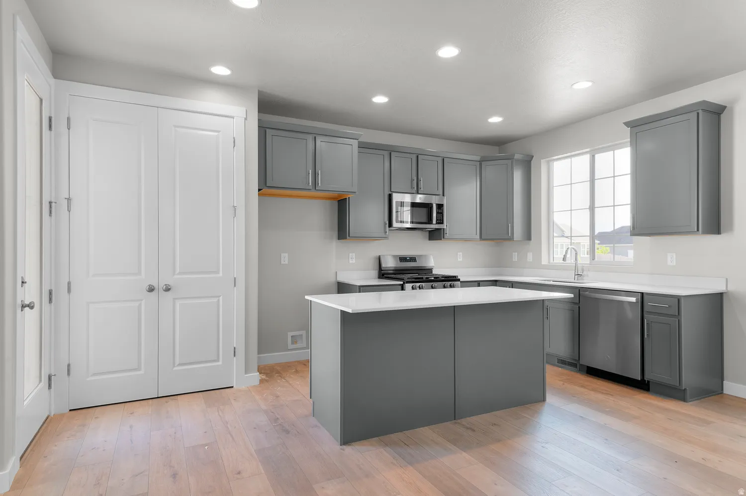 Contemporary kitchen featuring grey cabinetry, stainless steel appliances, a center island, and wood-finish flooring