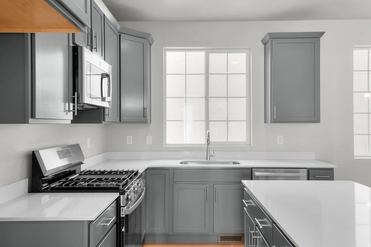 Modern kitchen featuring grey shaker-style cabinetry, white countertops, stainless steel appliances, and a central island