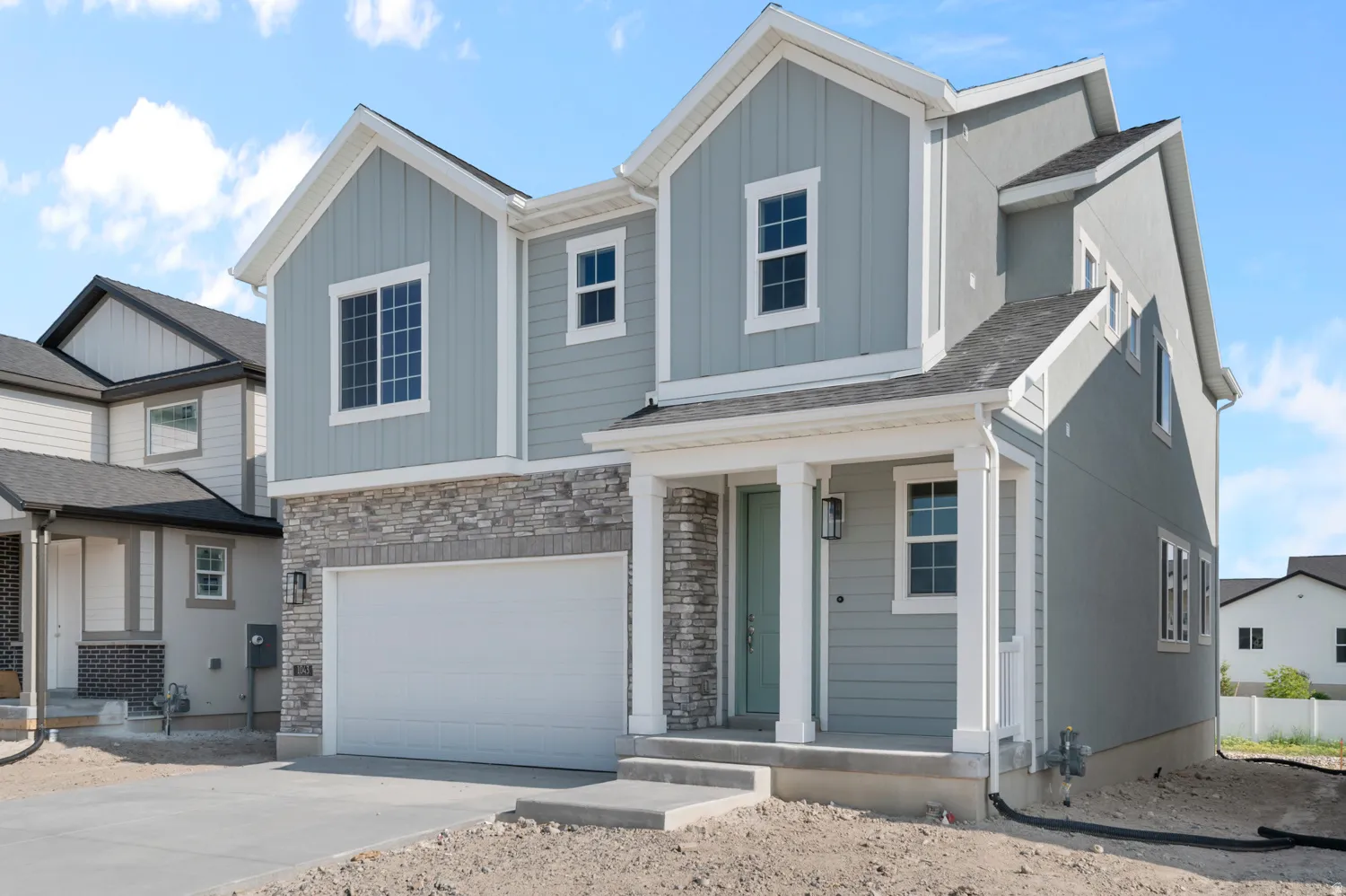 Two-story residence featuring light gray siding with board and batten accents, a stone facade, a two-car garage, and a covered porch with white columns