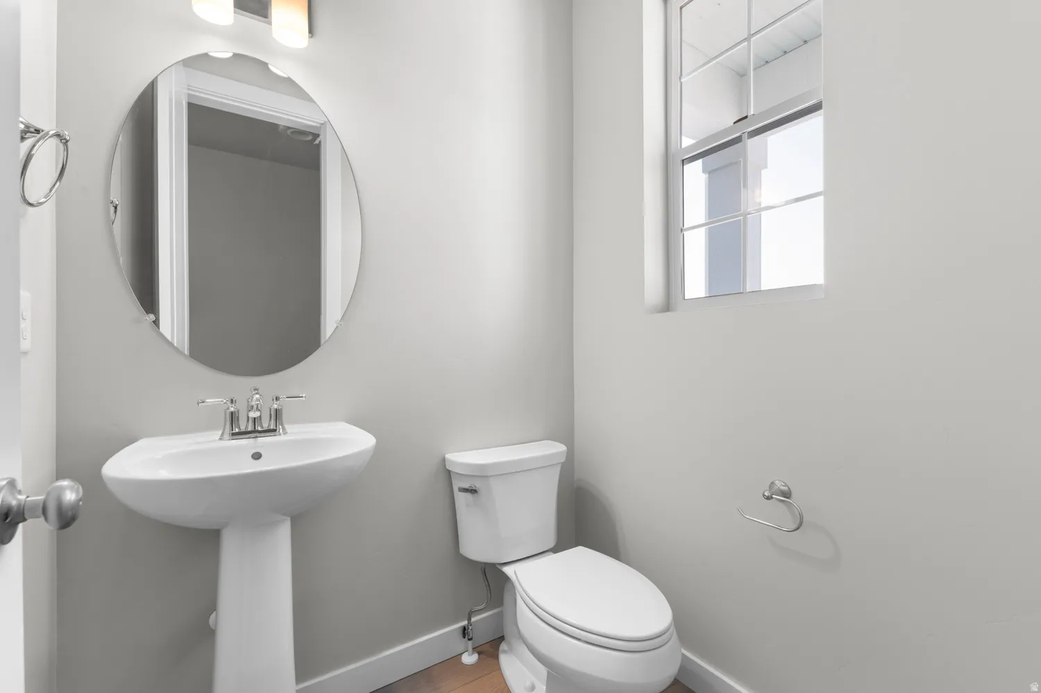 Bathroom featuring a pedestal sink with a chrome faucet, oval mirror, and a window with white trim