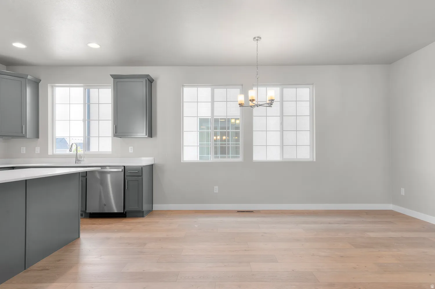 Open-concept living space with light wood-finish flooring, a contemporary chandelier, and multiple windows