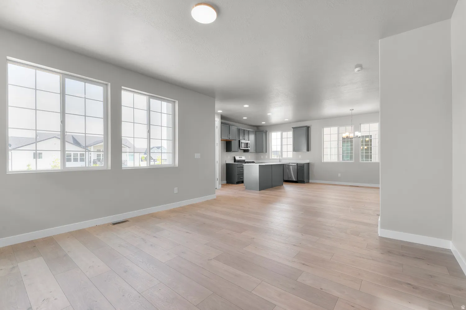 Open-concept living area featuring light wood-finish flooring, multiple grid-pattern windows, and recessed lighting