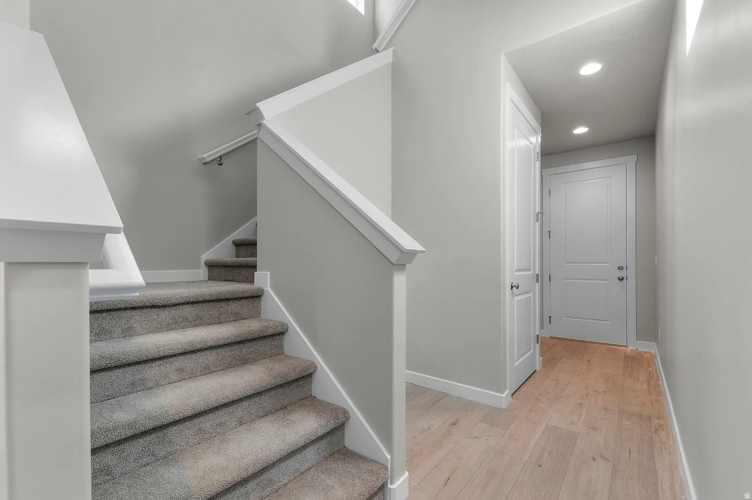Carpeted stairway with white risers and railing, light gray wall paint, wood-finish flooring, white paneled doors, and recessed ceiling lighting