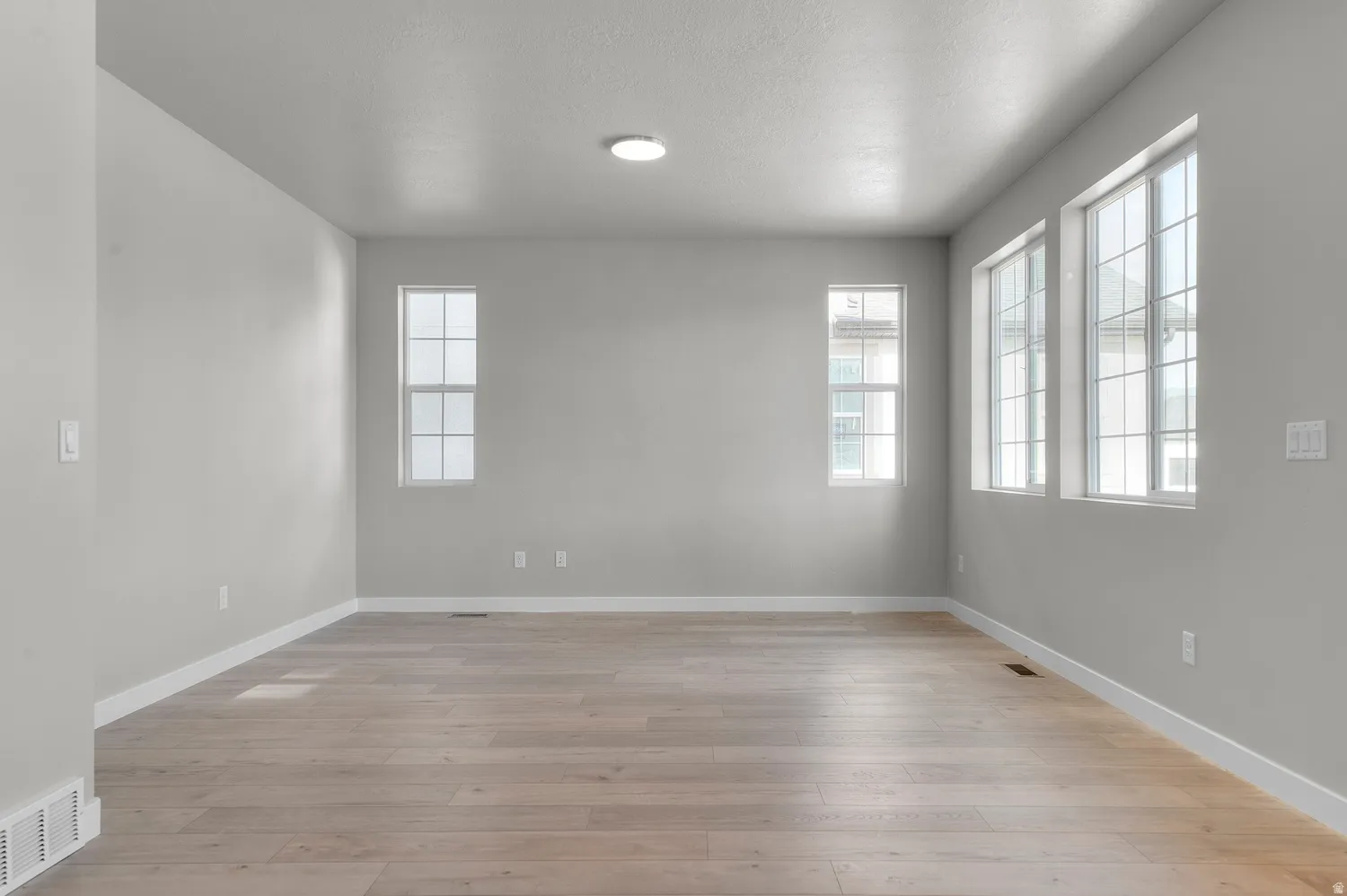 Spacious interior room featuring light wood-finish flooring, crisp white baseboards, and a neutral wall color