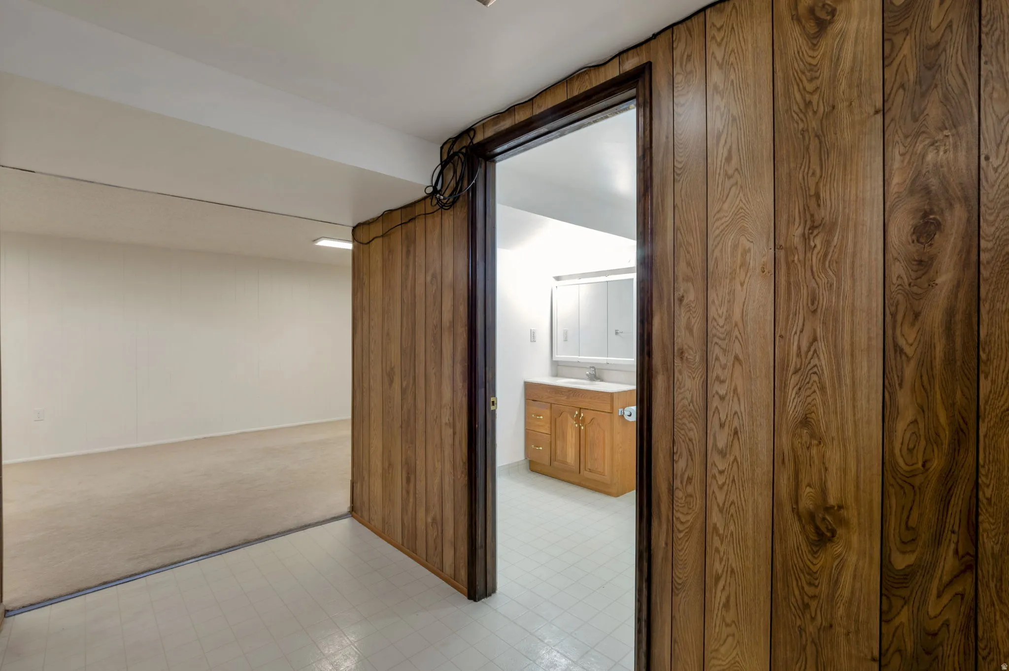 Wood-panel wall opening to a room featuring a vanity with a white countertop and a mirrored medicine cabinet
