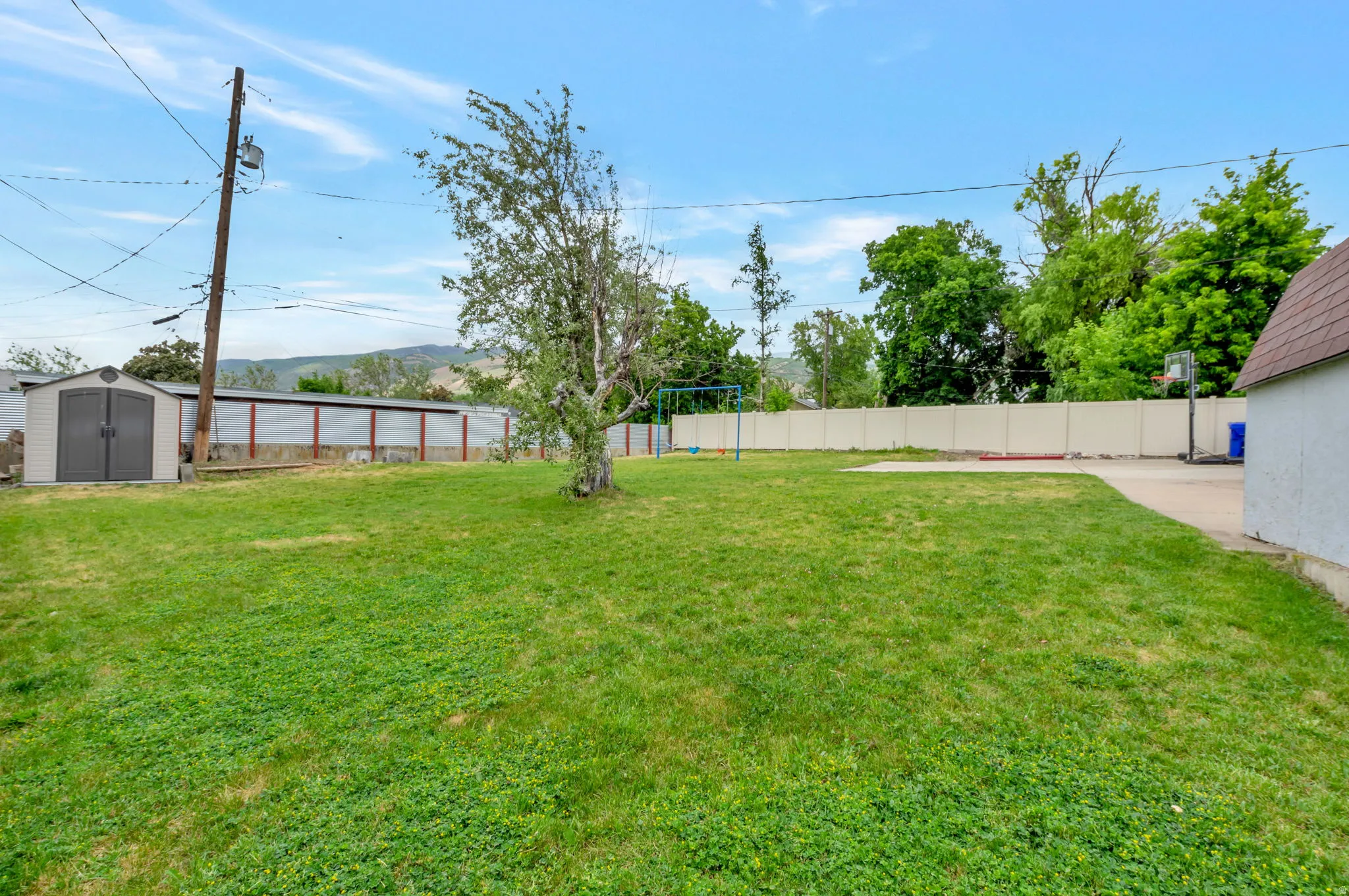 Expansive grassy backyard featuring a paved area, a storage shed, and perimeter fencing