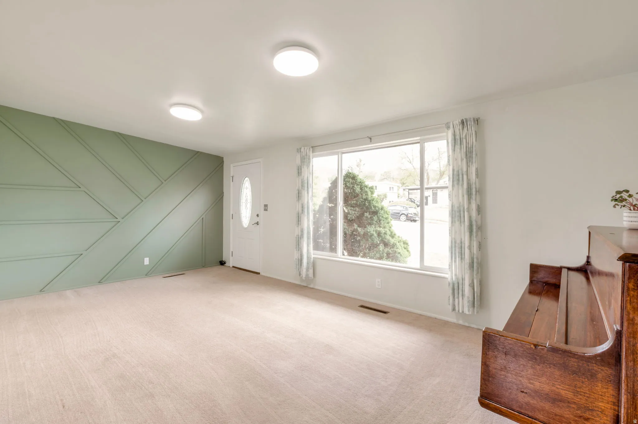 Spacious living area featuring a decorative accent wall, a white entry door with an oval glass insert, and large picture windows