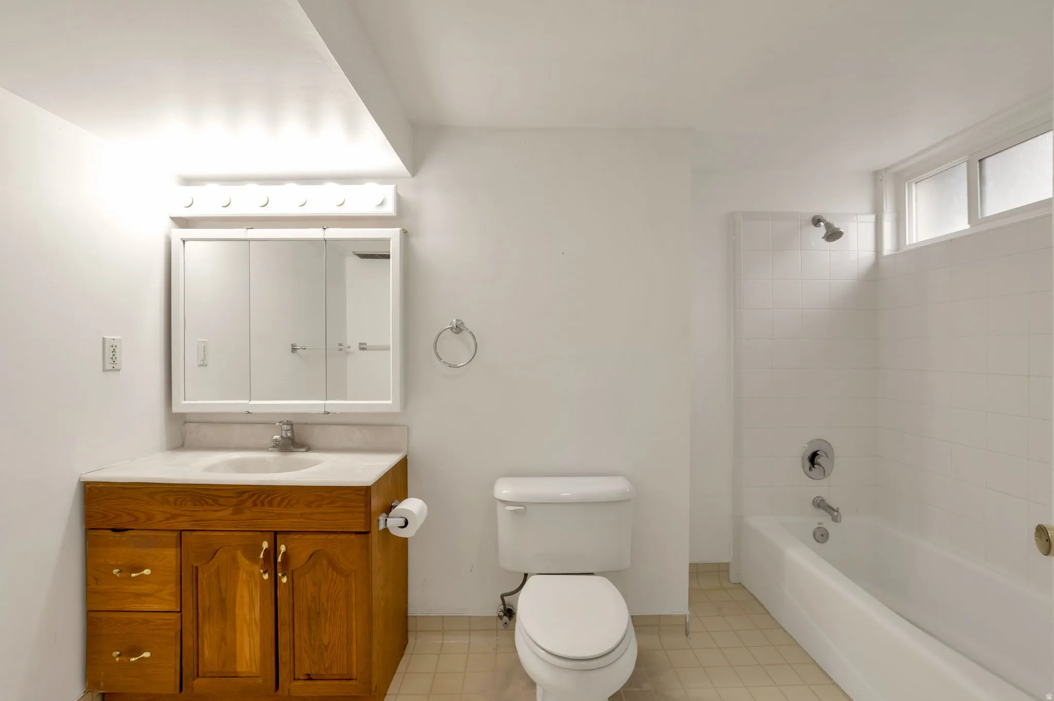 Bathroom featuring a wood-finish vanity with a built-in sink, a wall-mounted medicine cabinet with integrated mirror, and a full bathtub with a tiled shower surround