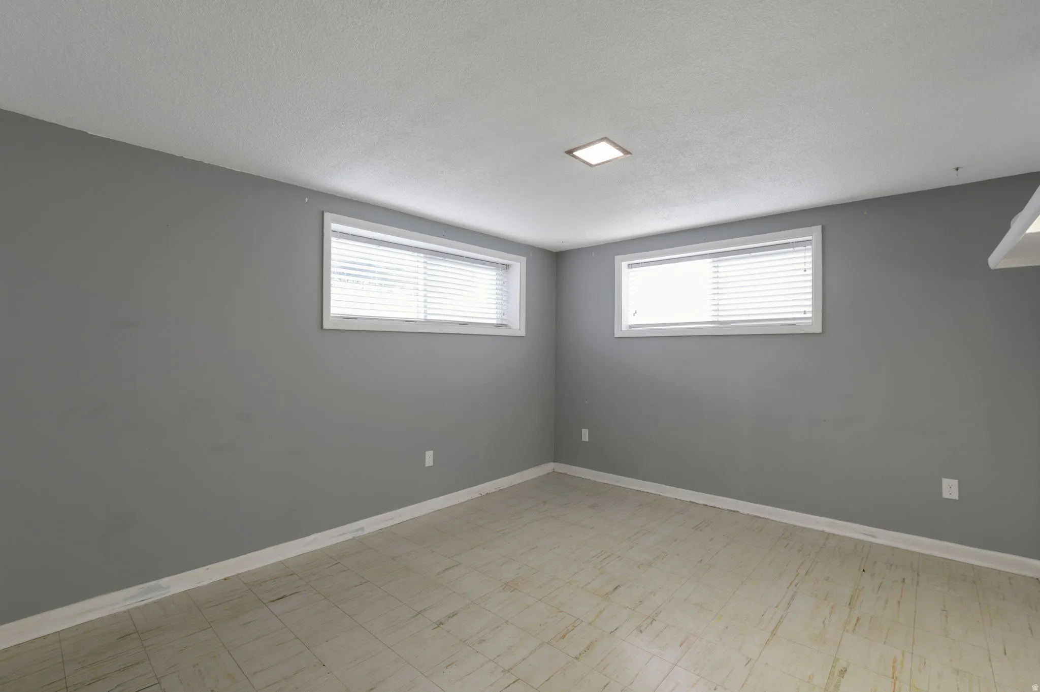 Room featuring light gray walls, two windows with white blinds, and light-colored tile flooring