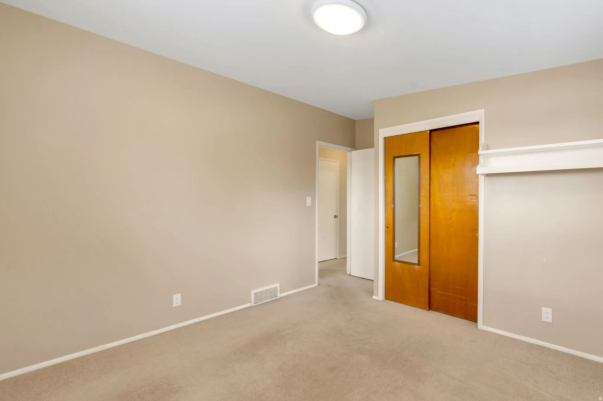 Carpeted room featuring a built-in closet with sliding wood-finish doors, one with an integrated mirror