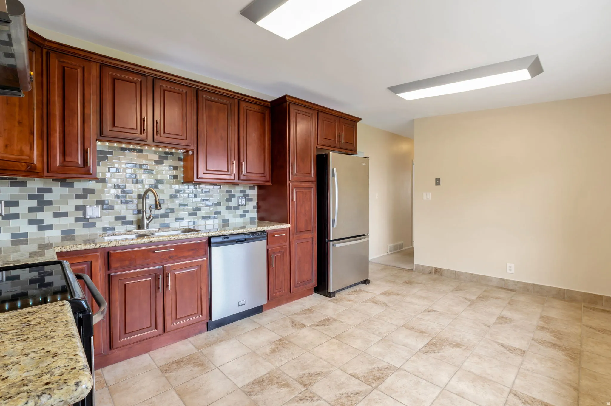 Kitchen featuring dark wood cabinetry, stainless steel appliances, granite countertops, and a mosaic tile backsplash