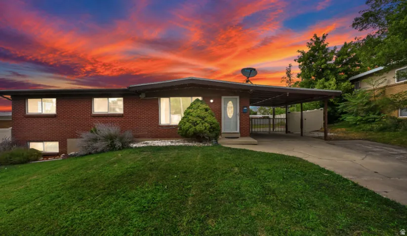 Brick exterior with a covered carport, mature front landscaping, and a sloped lawn