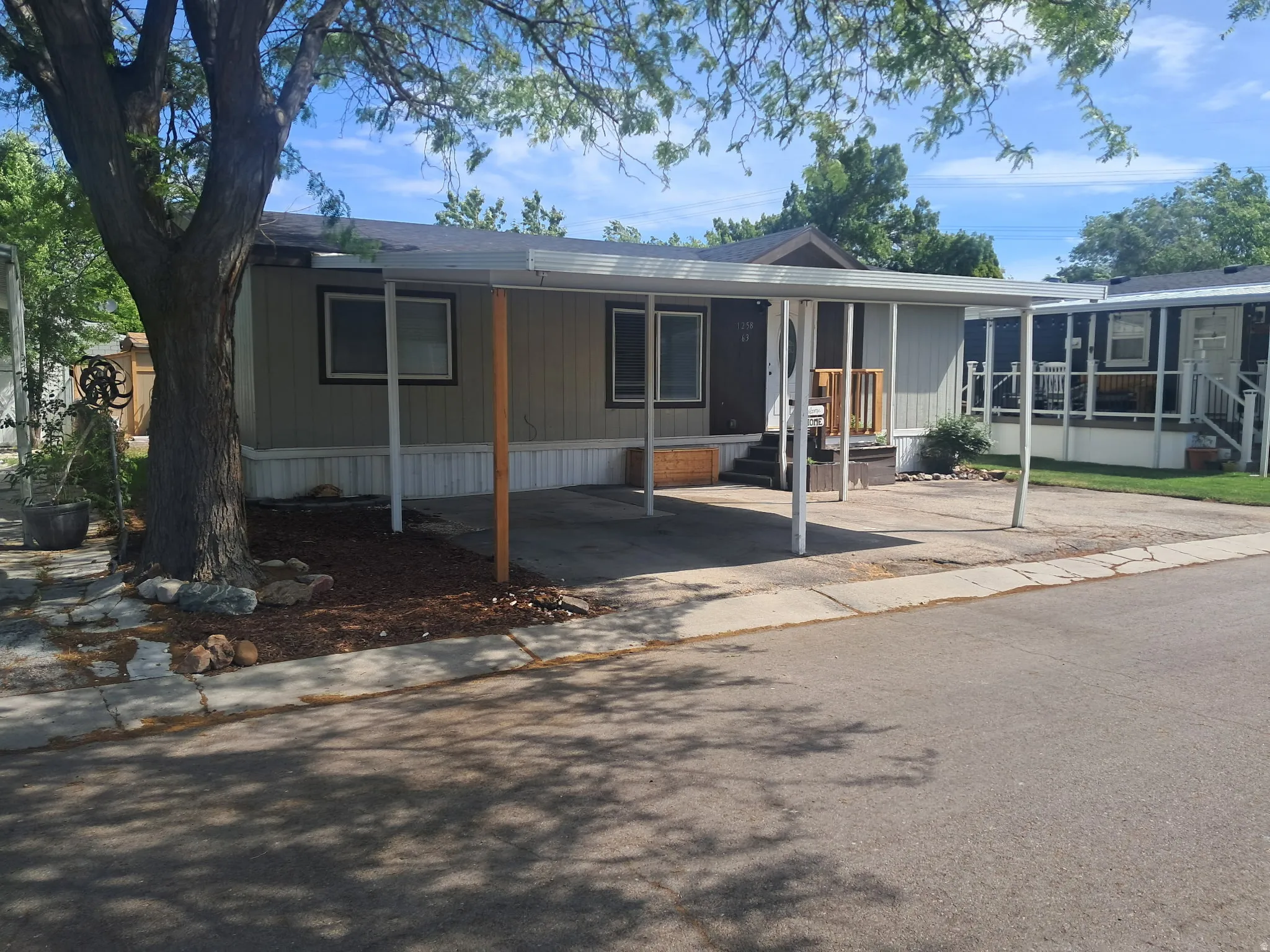 Single-story residence featuring a carport, light beige siding, and a dark brown front door with a small porch