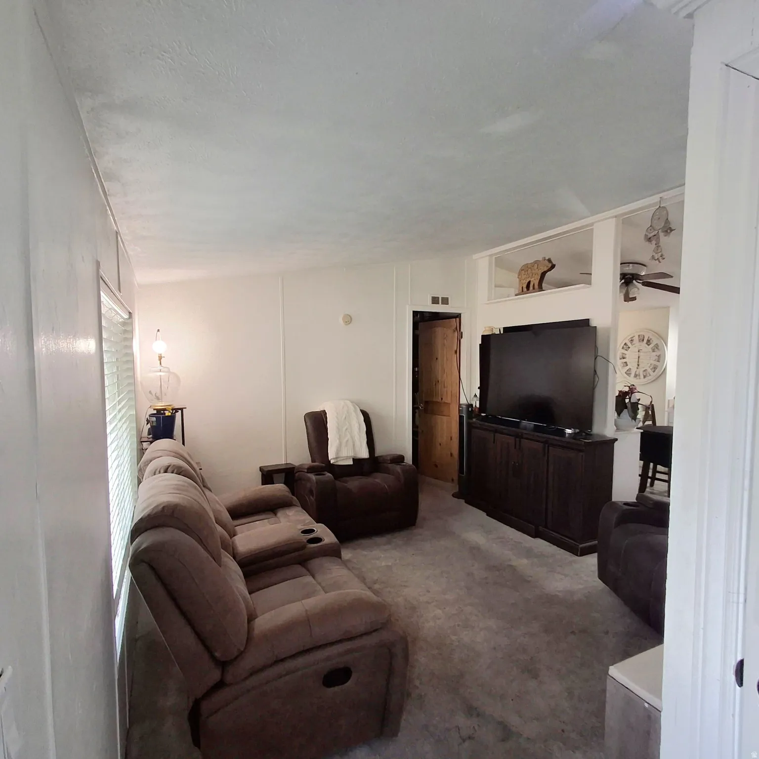 Living area featuring neutral wall finishes, light grey carpeting, window with blinds, and a built-in display shelf