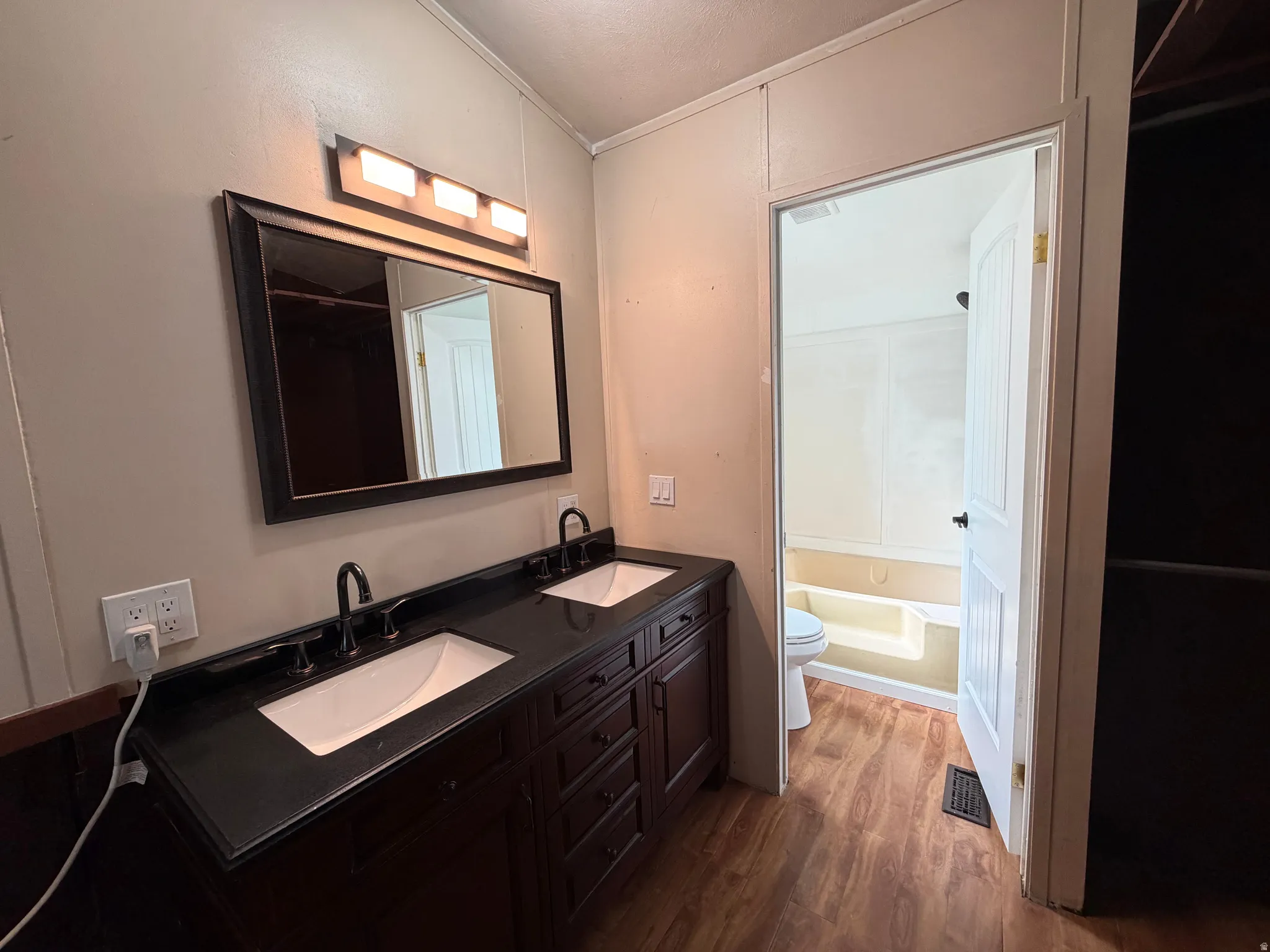 Dual vanity with dark cabinetry and countertop, framed mirror, and wood-finish flooring