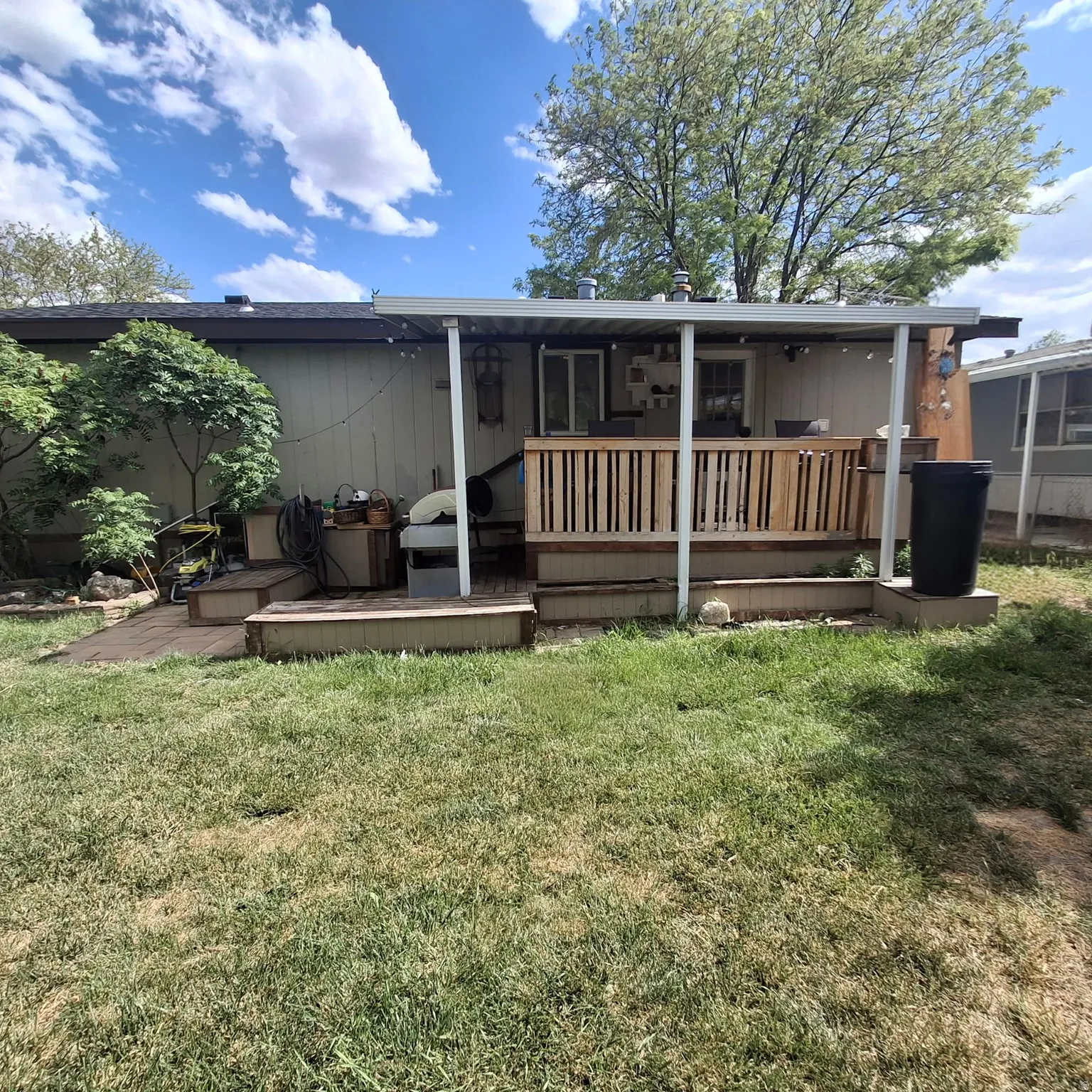 Rear exterior featuring a covered deck with wooden railing, multiple access points, and steps to a multi-level wooden patio