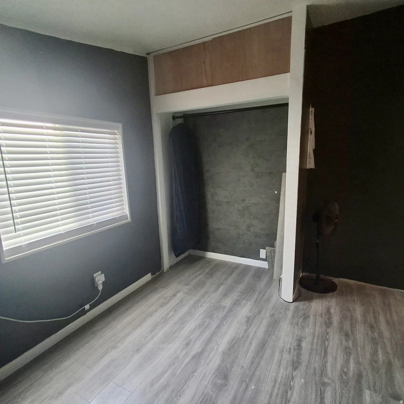 Room featuring wood-finish flooring, a window with horizontal blinds, and a built-in closet with a hanging rod