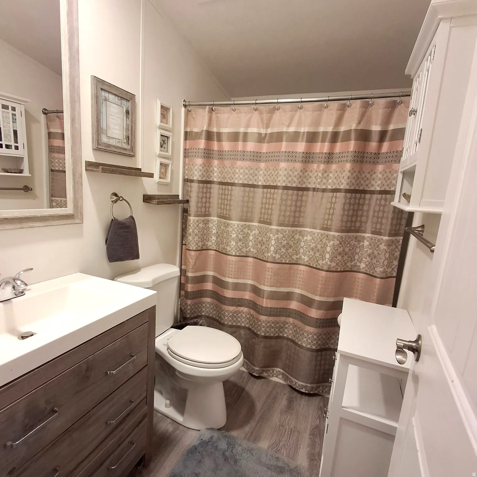 Bathroom featuring a wood-finish vanity with an integrated sink, white toilet, and wood-finish flooring