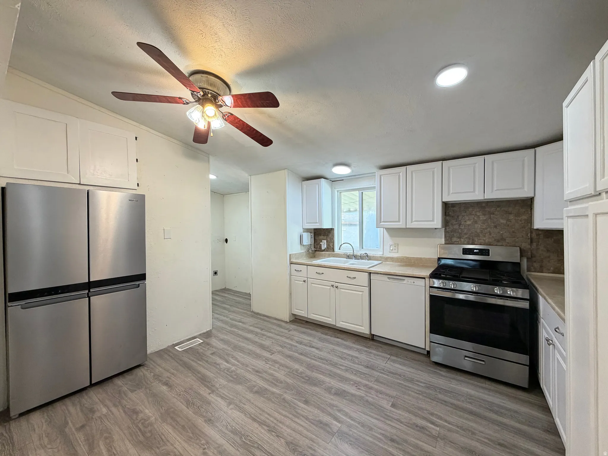Kitchen featuring wood-finish flooring, white cabinetry, stainless steel appliances, and recessed lighting