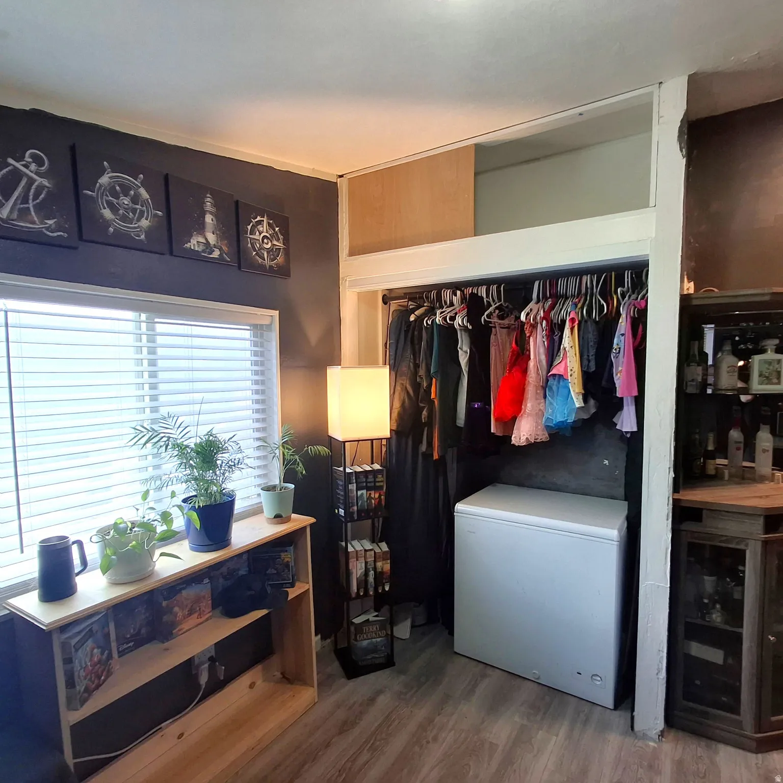 Room featuring wood-finish flooring, a window with horizontal blinds, and a built-in closet with overhead storage