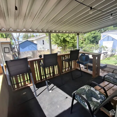 Covered outdoor patio featuring a slatted roof, integrated wooden bar with railing, string lighting, and a dark-toned floor surface