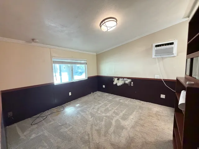 Window-mounted air conditioning unit, ceiling-mounted light fixture, light-colored carpeting, built-in shelving unit