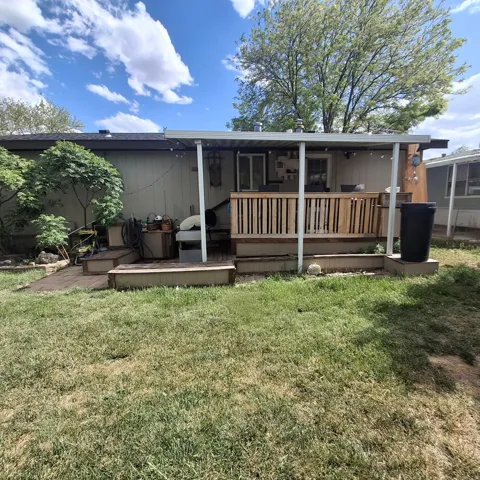 Rear exterior featuring a covered deck with wooden railing, multiple access points, and steps to a multi-level wooden patio