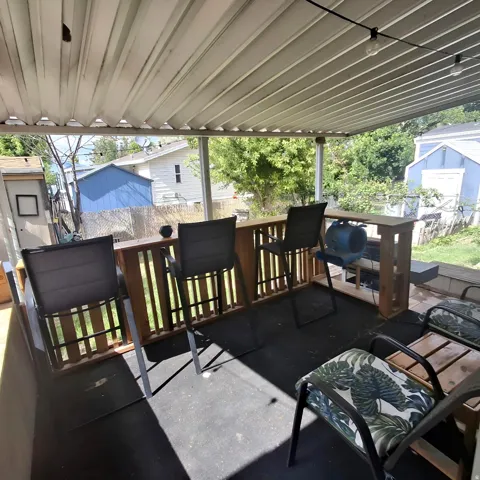 Covered outdoor patio featuring a slatted roof, integrated wooden bar with railing, string lighting, and a dark-toned floor surface